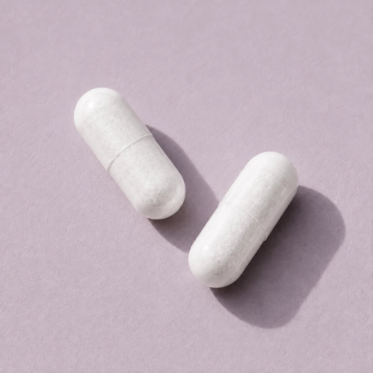 Two white vegetable capsules on a soft lavender background