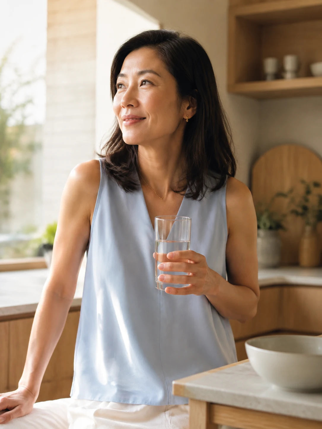 Illustrative lifestyle photo of a woman enjoying water in a sunlit kitchen